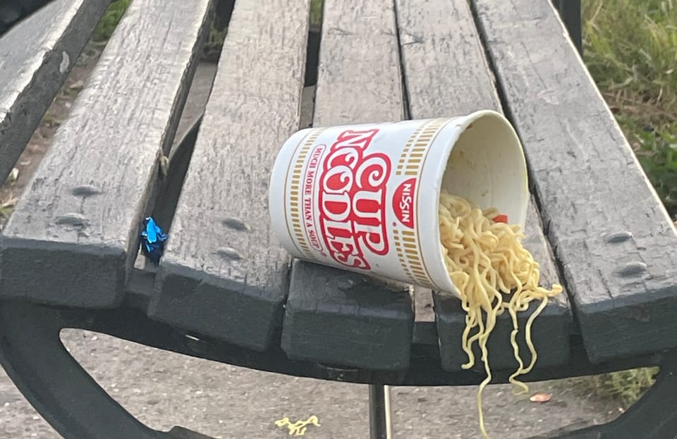 discarded cup noodles on park bench