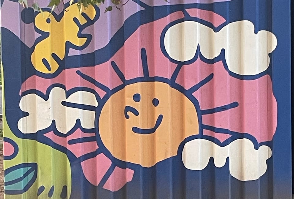 dumpster art: cartoonish sun, clouds and bird painted on the side of a dumpster.
