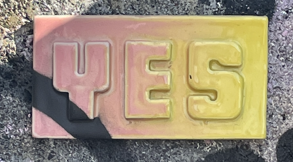 YES tile in pink & yellow affixed to a wall